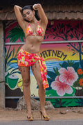 Woman in a colorful bikini and sarong posing in front of a vibrant mural.