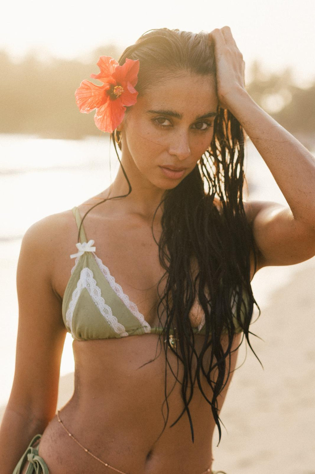 Woman in a green bikini with a red flower in her hair on a beach.
